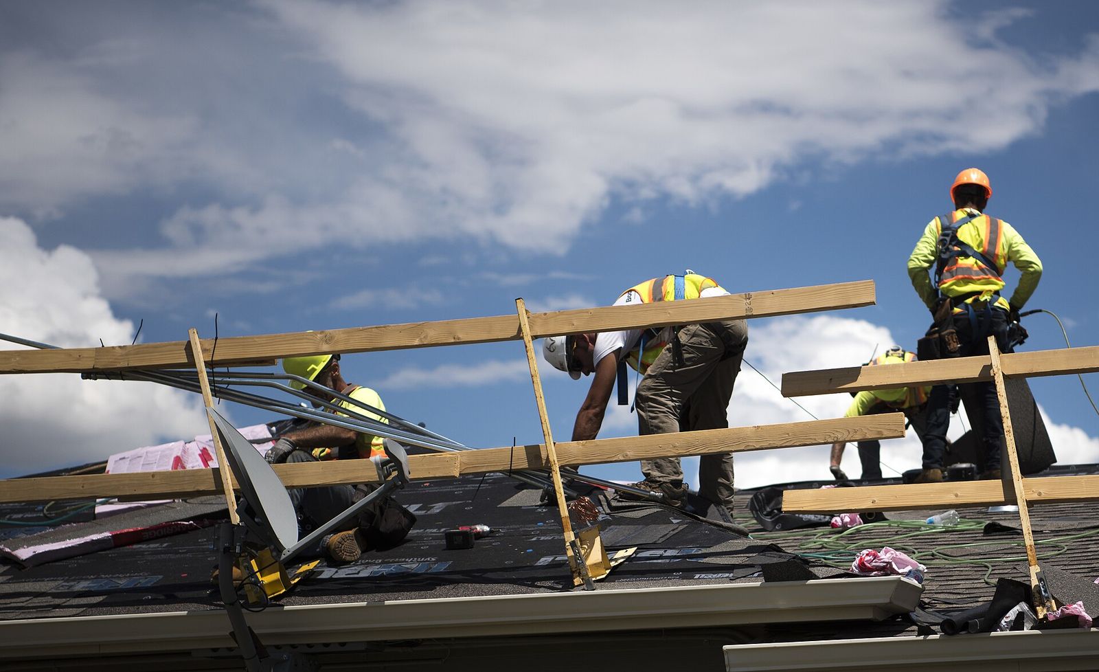 Roofing crew on a shingle roof under cloudy sky, mid tear-off