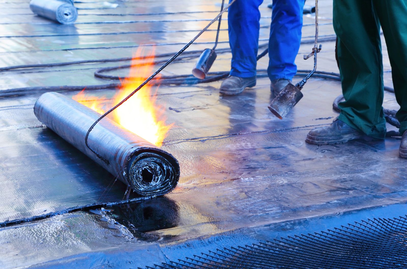 Roofer torching a roll of modified bitumen on a flat commercial roof